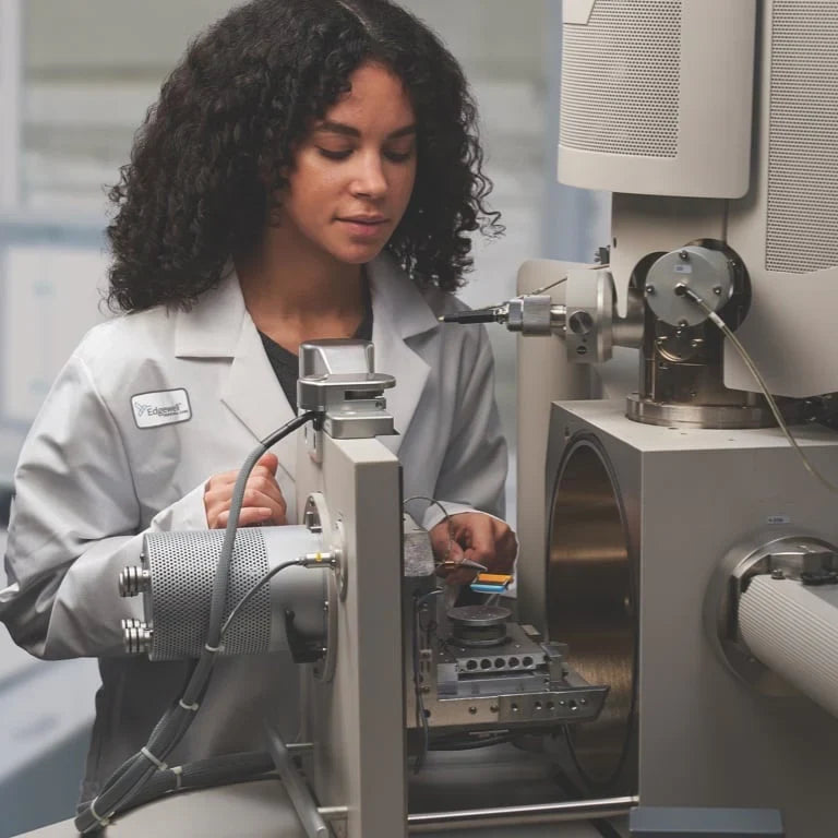 A woman in a white lab coat operating a large piece of industrial machinery in a clean, modern laboratory setting.