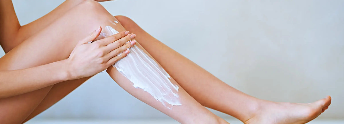 Person applying cream to their leg against a plain background